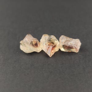 May include: Three sunstone crystals, each with a different shape and size. The crystals are translucent and have a golden-orange color with a hint of red.
