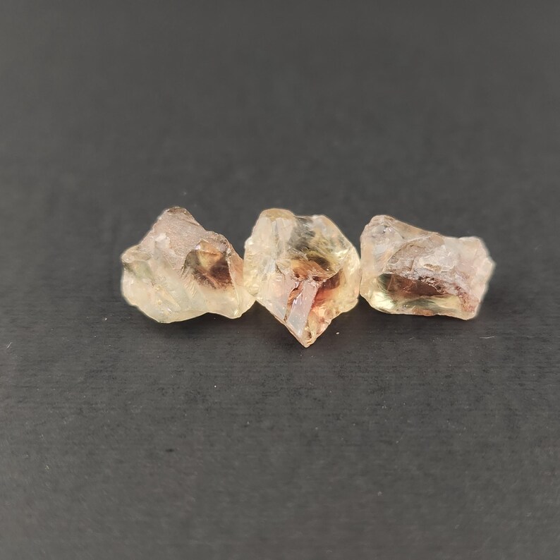 May include: Three sunstone crystals, each with a different shape and size. The crystals are translucent and have a golden-orange color with a hint of red.
