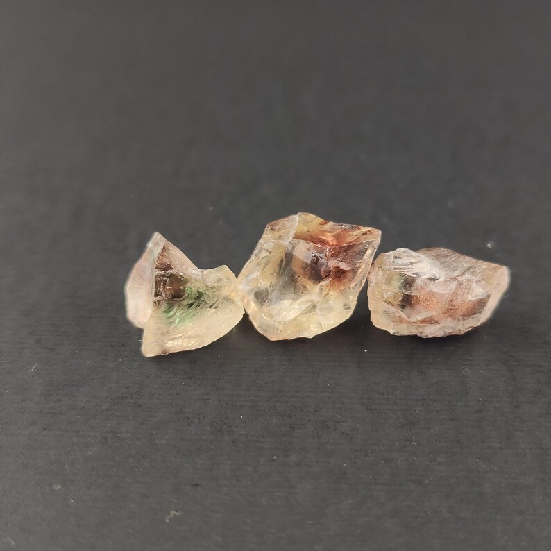 May include: Three sunstone crystals, each with a different color and pattern. The crystals are translucent and have a variety of colors, including green, red, and orange.