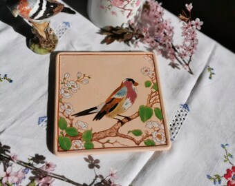 Dessous de plat Longwy beige rose avec un décor de bouvreuil pivoine sur une branche de cerisier en fleur. Motif délicat d'oiseau peint.