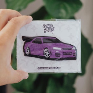 May include: Purple embroidered iron-on patch of a car with the text "Run the Streets" and "@runthestreets.shop" on a white background.