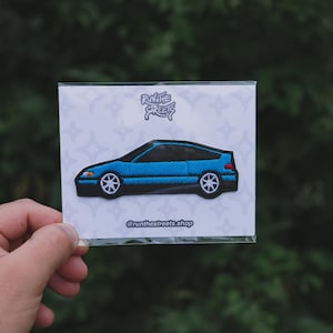 May include: A blue embroidered patch of a Honda Civic Del Sol with the text "Run the Streets" and the social media handle "@runthestreets.shop" printed below the car.