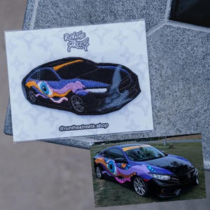 May include: A black car with a custom paint job featuring a large eye design in purple, blue, and orange. The car is a Honda Civic with a black spoiler and a yellow stripe on the hood. The image also includes a smaller version of the car as a patch with the text "Run the Streets" and "@runthestreets.shop".