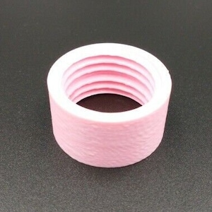 Puede incluir: Un anillo de plástico rosa con una superficie texturizada y múltiples ranuras en el interior.