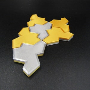 Puede incluir: Un rompecabezas geométrico hecho de piezas que encajan. El rompecabezas está hecho de dos colores: plata y oro. Las piezas están dispuestas en un patrón que se asemeja a una flor.