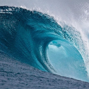 Puede incluir: Primer plano de una gran ola oceánica rompiendo. La ola es de un color turquesa profundo, con una cresta blanca y espumosa. La luz del sol ilumina el agua, creando una sensación de movimiento y poder.