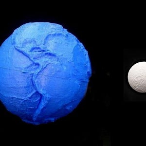 May include: A blue, textured sphere, reminiscent of a planet, with visible continents and a thin line around it. Next to it, a white, textured sphere, perhaps a moon, is set against a black background.