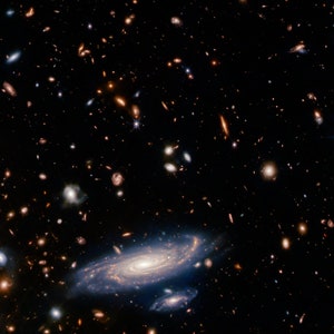 May include: A deep space image showing a vast expanse of stars and galaxies. A spiral galaxy is visible in the center of the image, with other galaxies scattered throughout the background.