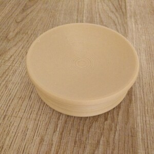 May include: A beige ceramic bowl with a circular, slightly raised rim and a textured, concentric circle pattern on the inside.