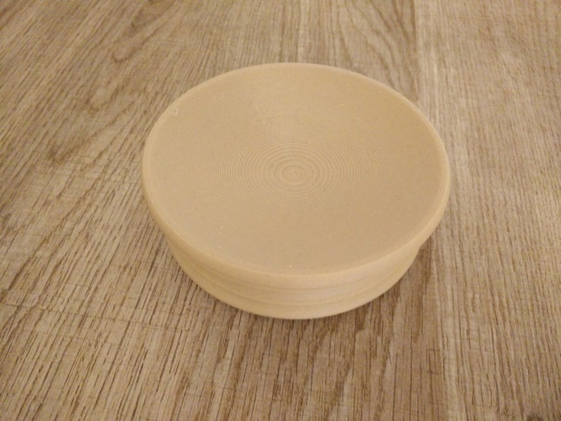 May include: A beige ceramic bowl with a circular, slightly raised rim and a textured, concentric circle pattern on the inside.