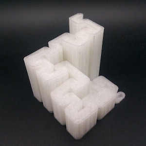 Puede incluir: Objeto blanco impreso en 3D con un diseño geométrico complejo. El objeto está formado por múltiples piezas que se entrelazan, creando una estructura única e intrincada.