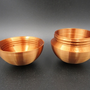 Op de afbeelding: Een koperkleurige, 3D-geprinte, bolvormige container met een deksel. De container is open en het deksel ligt ernaast.