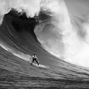 Może przedstawiać: Surfer jedzie na dużej fali, woda jest biała i pienista, surfer ma na sobie piankę i trzyma deskę surfingową.