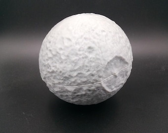 May include: A white, spherical object with a textured surface, resembling the moon. The sphere has craters and a seam running around its circumference. The object is set against a dark background.