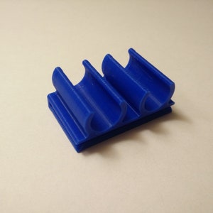 K&ouml;nnte beinhalten: Ein blauer Kabelorganizer aus Kunststoff mit zwei Schlitzen zum Halten von Kabeln.