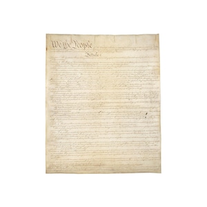 May include: A parchment document with the words "We the People" at the top, and the text of Article 1 below. The document is aged, with visible creases and a yellowed hue, suggesting historical significance.