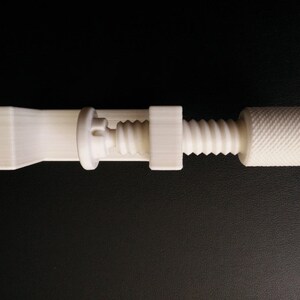 May include: A white plastic clamp with a screw mechanism. The clamp has a long, flat base and a threaded screw with a knob on the end.