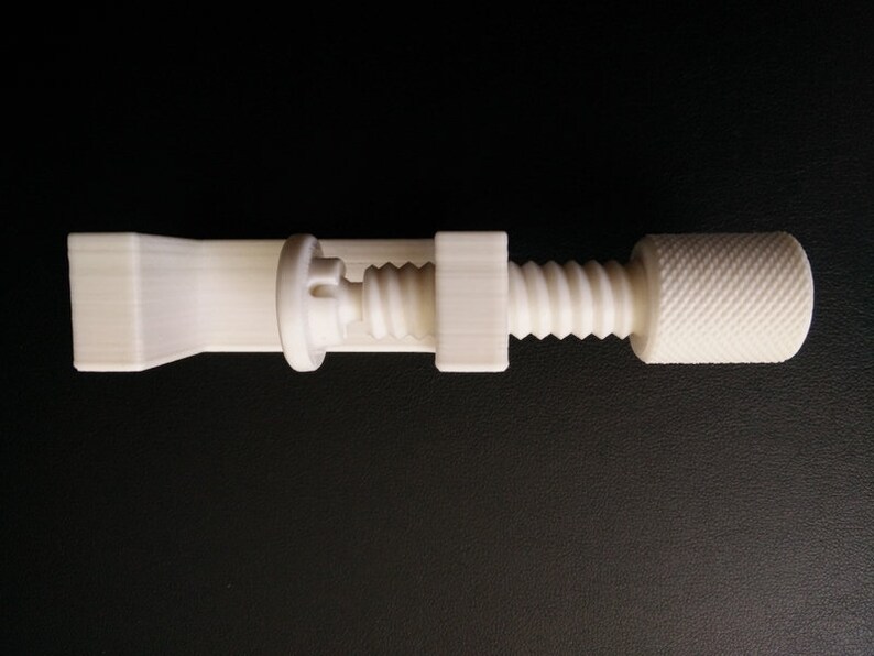 May include: A white plastic clamp with a screw mechanism. The clamp has a long, flat base and a threaded screw with a knob on the end.