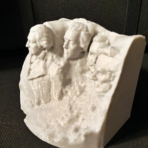 Pu&ograve; includere: Un modello in 3D stampato in bianco del Monte Rushmore, con i volti di quattro presidenti scolpiti sul fianco di una montagna.