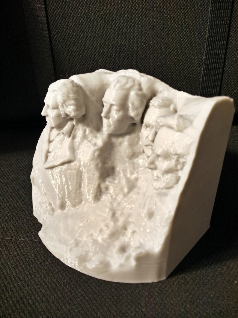 Pu&ograve; includere: Un modello in 3D stampato in bianco del Monte Rushmore, con i volti di quattro presidenti scolpiti sul fianco di una montagna.