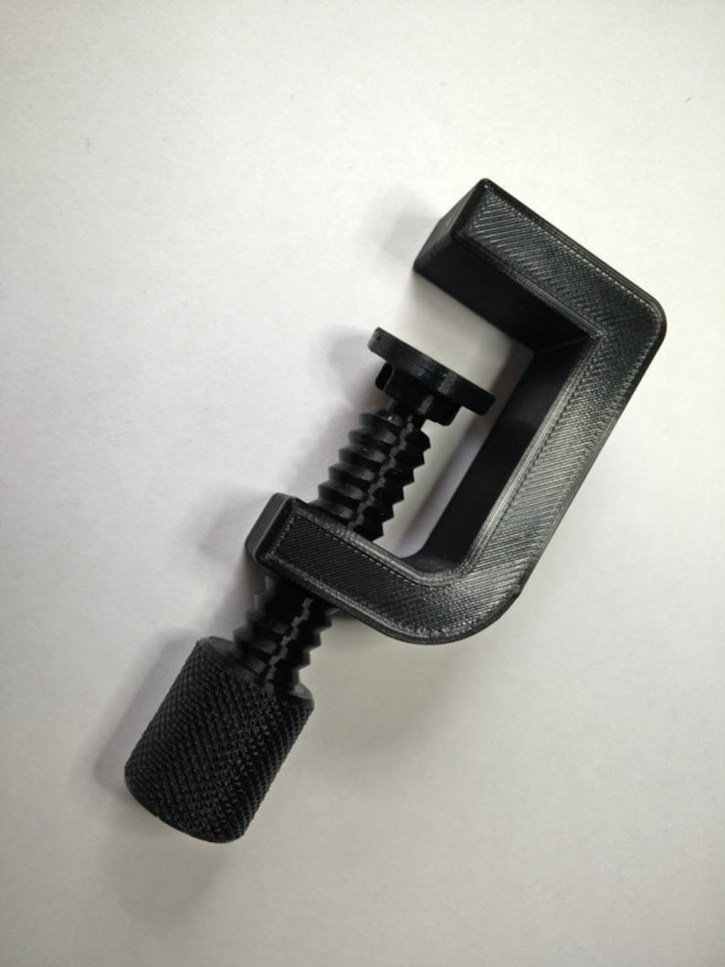 May include: A black plastic clamp with a threaded screw and a knob. The clamp is designed to hold objects together.