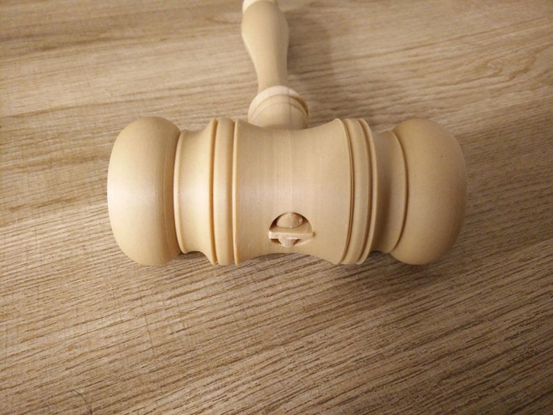 May include: A wooden gavel with a carved design on the side. The gavel is light brown in color and has a smooth finish.