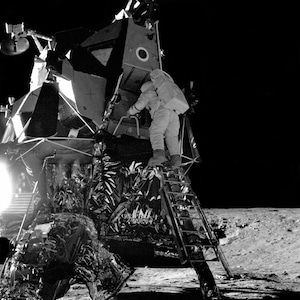 May include: A black and white photo of an astronaut climbing a ladder to enter a lunar module on the moon.