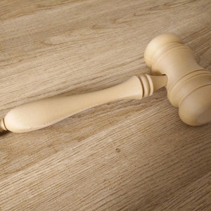 May include: A wooden gavel with a light brown finish. The gavel has a rounded head and a long handle.