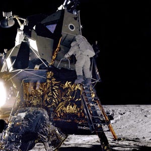 May include: A black and white photo of an astronaut climbing a ladder to enter a lunar module on the moon. The lunar module is covered in a gold-colored material.