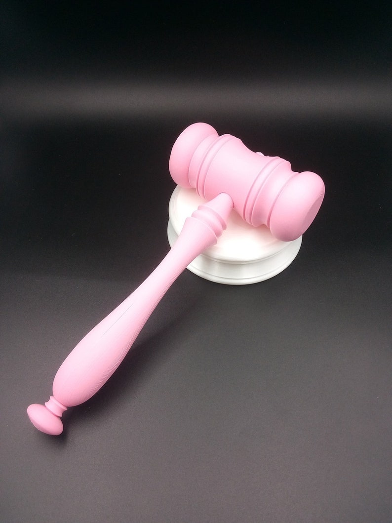 May include: A pink wooden gavel with a white base. The gavel is a traditional symbol of authority and is often used in courtrooms.
