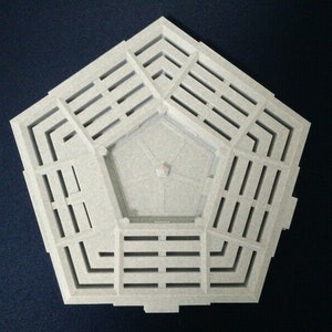 May include: A white, pentagonal-shaped, decorative object with a central, raised, pentagonal section and a series of concentric, rectangular cutouts around the perimeter.