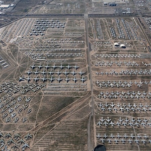 Peut inclure: Vue aérienne d'un grand cimetière d'avions avec des centaines d'avions militaires retirés du service alignés en rangées. Les avions sont principalement gris et blancs, et ils sont garés sur un terrain en terre.