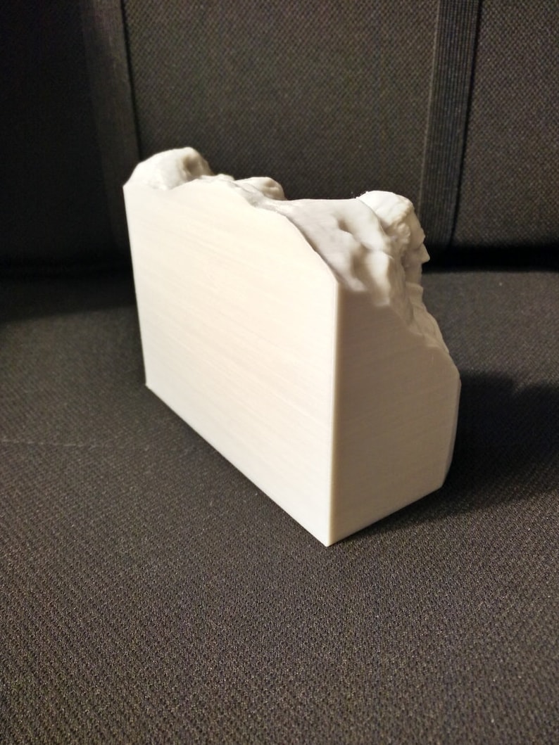 Pu&ograve; includere: Una scultura bianca stampata in 3D di una formazione rocciosa. La scultura &egrave; su una superficie testurizzata grigio scuro.