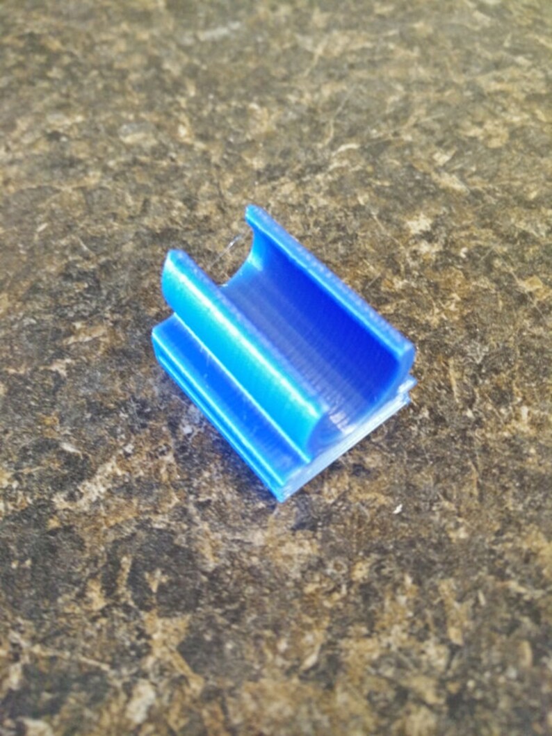 K&ouml;nnte beinhalten: Ein kleines, blaues Plastikteil mit einem Kanal, der durchl&auml;uft. Das Teil ist so konzipiert, dass es als Verbinder oder F&uuml;hrung verwendet werden kann.