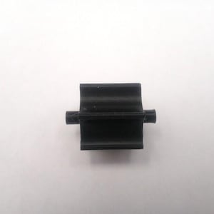 May include: A small, black plastic component with a rectangular body and two cylindrical protrusions extending from the sides. The object is set against a plain white background, highlighting its shape and form.