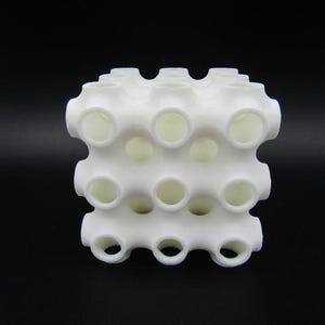 Op de afbeelding: Een wit 3D-geprint object met een honingraatontwerp. Het object heeft meerdere ronde gaten over het hele oppervlak.