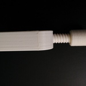 May include: A white plastic clamp with a threaded screw and a knob. The clamp is designed to hold objects together.