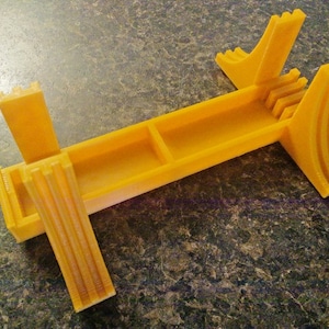 Peut inclure: Un support en plastique jaune avec une base rectangulaire et deux supports verticaux. Le support a une fente au milieu pour maintenir des objets.
