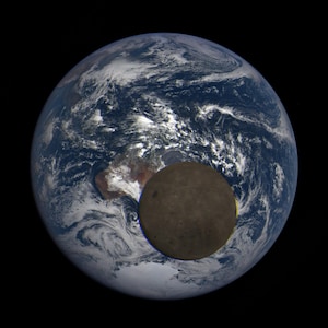 May include: A photograph of Earth from space, with the moon partially eclipsing the planet. The moon appears dark gray and is positioned in the lower right corner of the image. The Earth is mostly blue with white clouds.