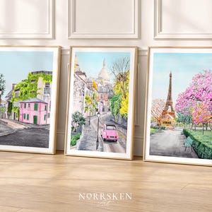 May include: Three framed watercolor prints depicting Parisian street scenes. One features a pink building covered in ivy, another a pink car on a cobblestone street, and the last the Eiffel Tower with pink flowering trees.