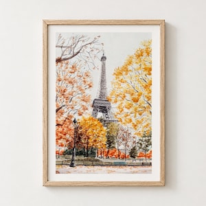 Puede incluir: Una lámina de acuarela enmarcada que representa la Torre Eiffel de París rodeada de árboles otoñales con follaje naranja y amarillo brillante. Una farola negra se alza en primer plano junto a un banco, con hojas caídas en el suelo.