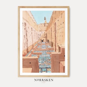 May include: A framed watercolor print depicting a narrow courtyard with tall, tan-colored earthen walls and intricate blue and white geometric tile patterns on the ground. The scene features a light blue sky above and the text NORRSKEN Art below.