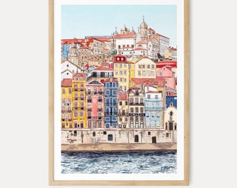 May include: A framed watercolour print depicting a European city with vibrant buildings and red-tiled roofs. The artwork, set in a light wood frame, shows a river in the foreground. The print is signed "NORRSKEN Art" at the bottom.