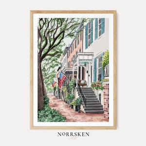 May include: A watercolor art print depicting a street scene with historic townhouses, a large tree, and American flags. The buildings feature light-colored facades, blue shutters, and brick steps leading to porches. The text NORRSKEN Art is at the bottom.