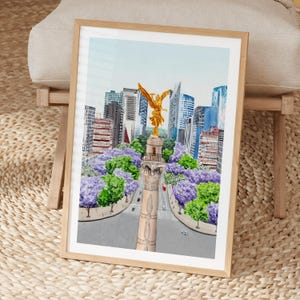 Può includere: Stampa ad acquerello di un paesaggio urbano con una statua dorata in cima a una colonna, circondata da alberi viola e verdi. Alti edifici e un cielo azzurro chiaro fanno da sfondo, incorniciati in legno chiaro. L'opera cattura una vivace scena urbana.