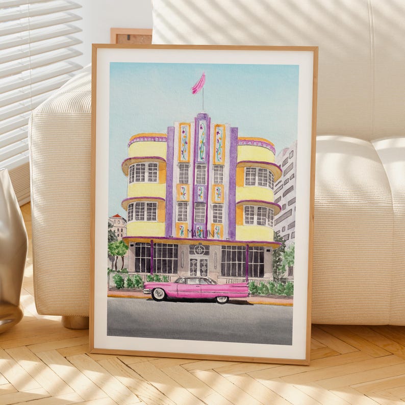 May include: A watercolor art print featuring a yellow and purple Art Deco building with the word MARLIN visible on the facade. A vintage pink car is parked in front of the building on a gray street. The sky is a light blue with a pink flag on top.
