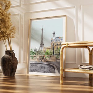 May include: Framed watercolor print of the Eiffel Tower in Paris, France. The artwork features a bicycle, street lamp, and buildings. The print is displayed in a room with a wooden floor and a decorative vase.