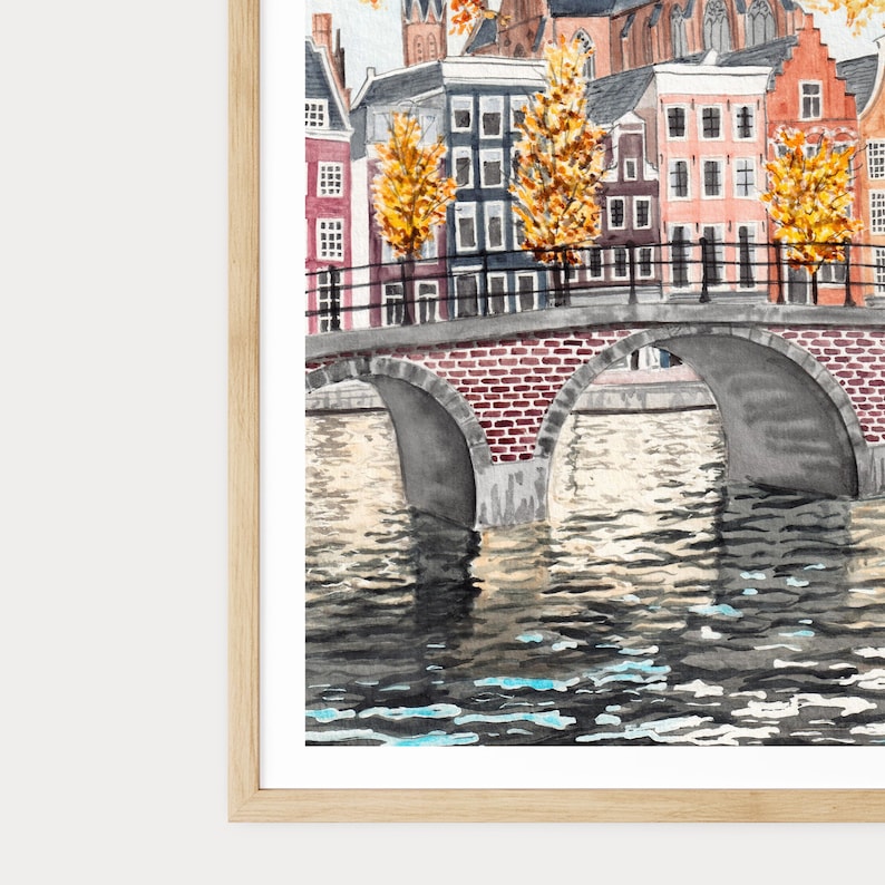 May include: Watercolour painting of a European cityscape with a brick bridge over a canal. Buildings of various styles line the canal, with autumn trees adding yellow and orange. The water reflects the buildings and sky.