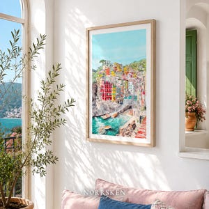 May include: A framed vertical wall art print featuring a watercolour painting of a coastal Italian village with colourful buildings stacked on a cliffside, overlooking a turquoise harbour with small boats, all set against a bright blue sky.