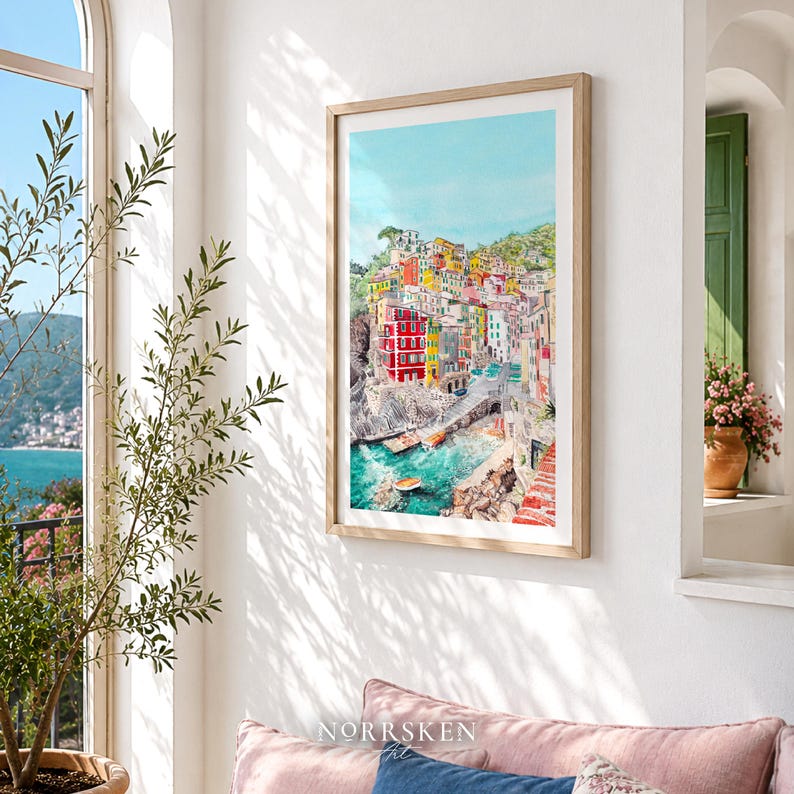 May include: A framed vertical wall art print featuring a watercolour painting of a coastal Italian village with colourful buildings stacked on a cliffside, overlooking a turquoise harbour with small boats, all set against a bright blue sky.